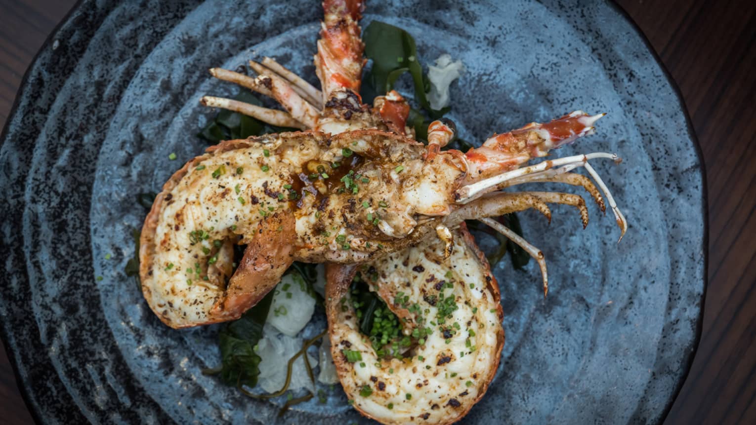 Roasted spiny lobster sprinkled with herbs on stone-like plate