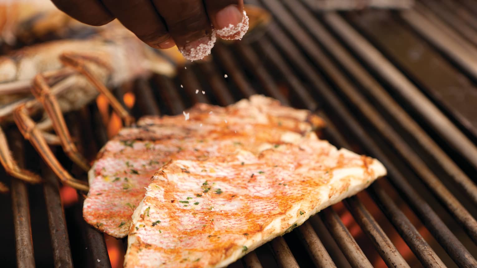 Close-up of hands sprinkling salt garnish on grilled fish on barbecue