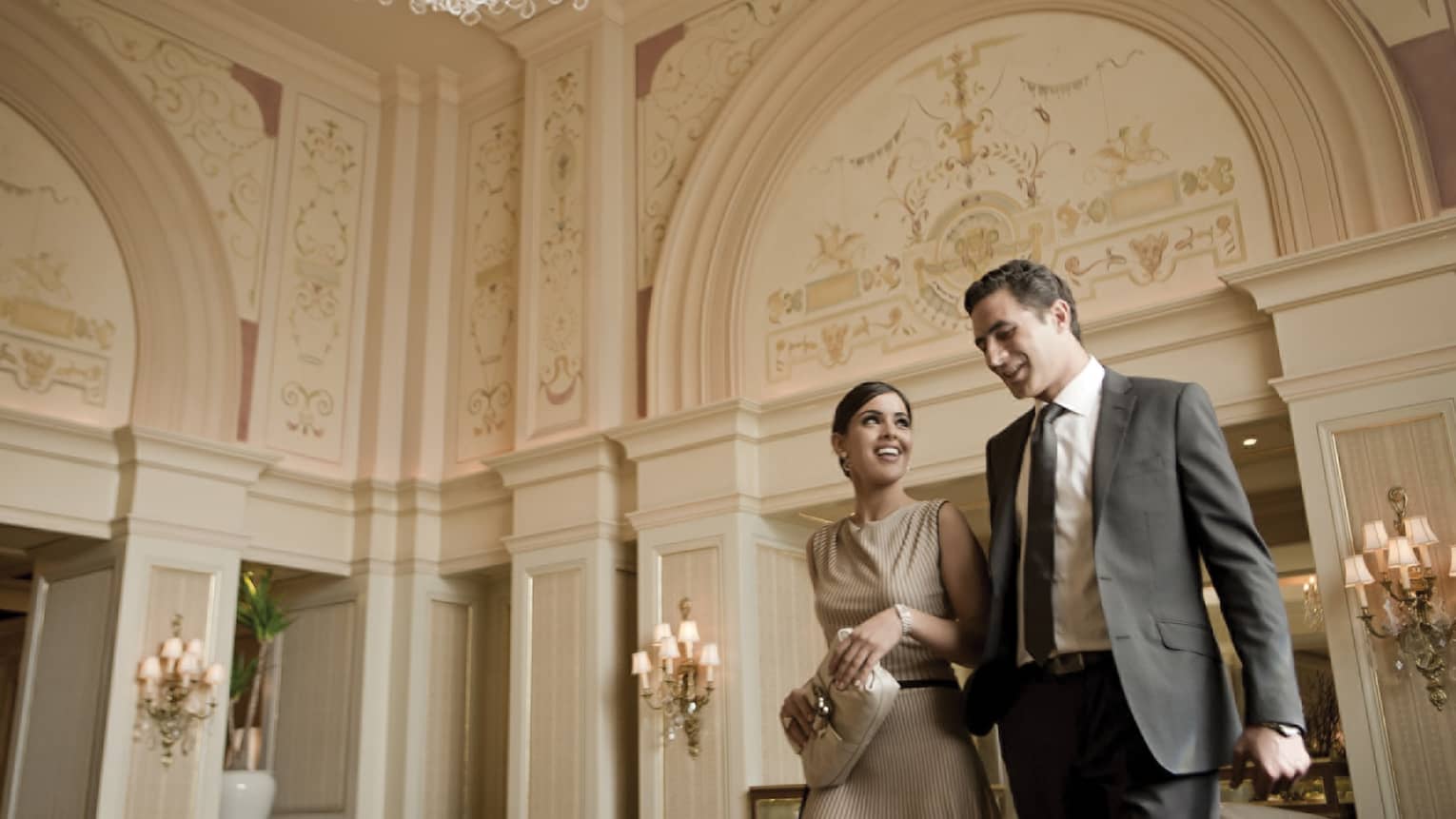 Smiling woman and man in business attire walk through hotel lobby