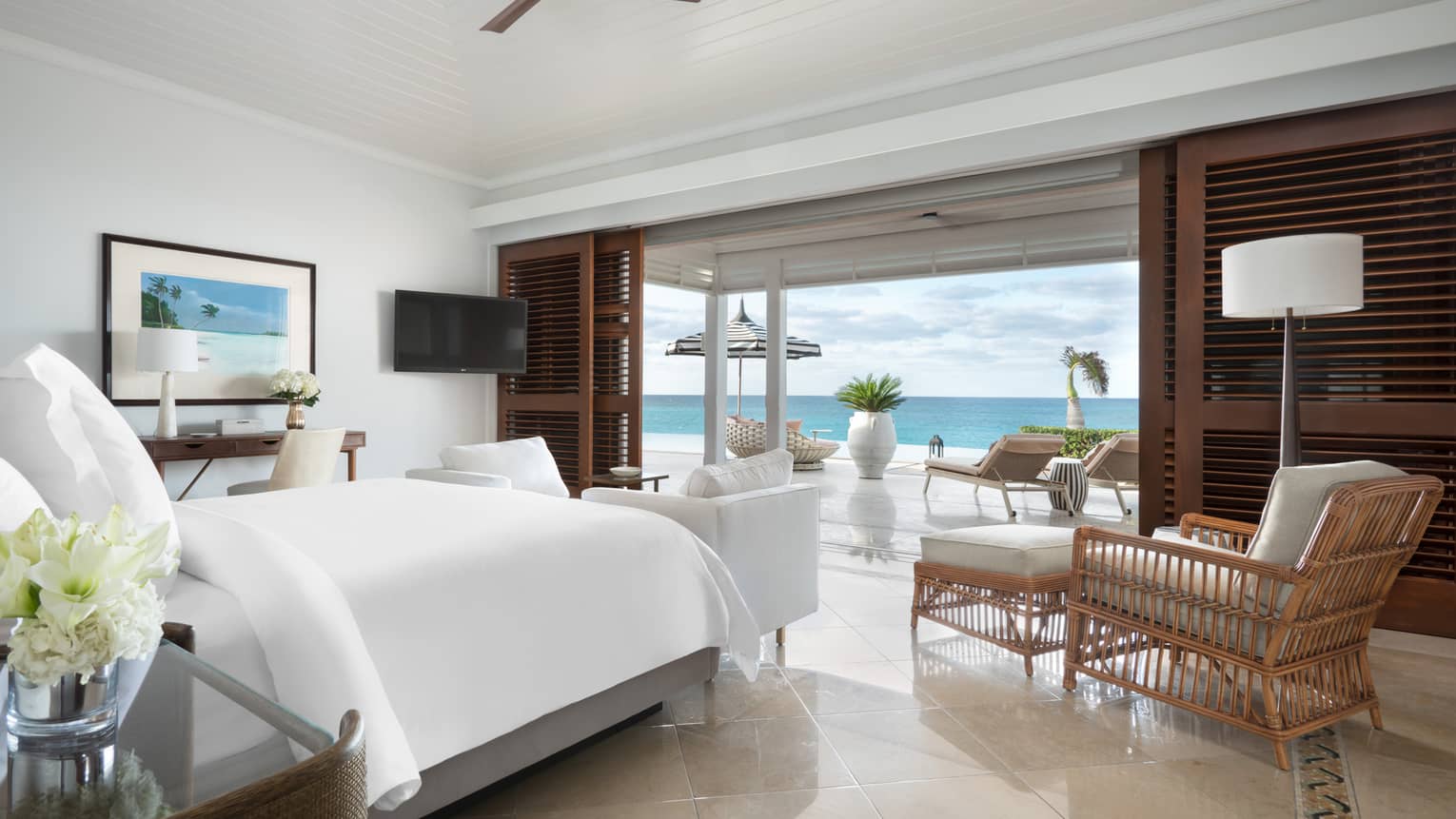 Beachfront villa residence bedroom with a bed, cozy seating area and a private terrace with loungers overlooking the ocean