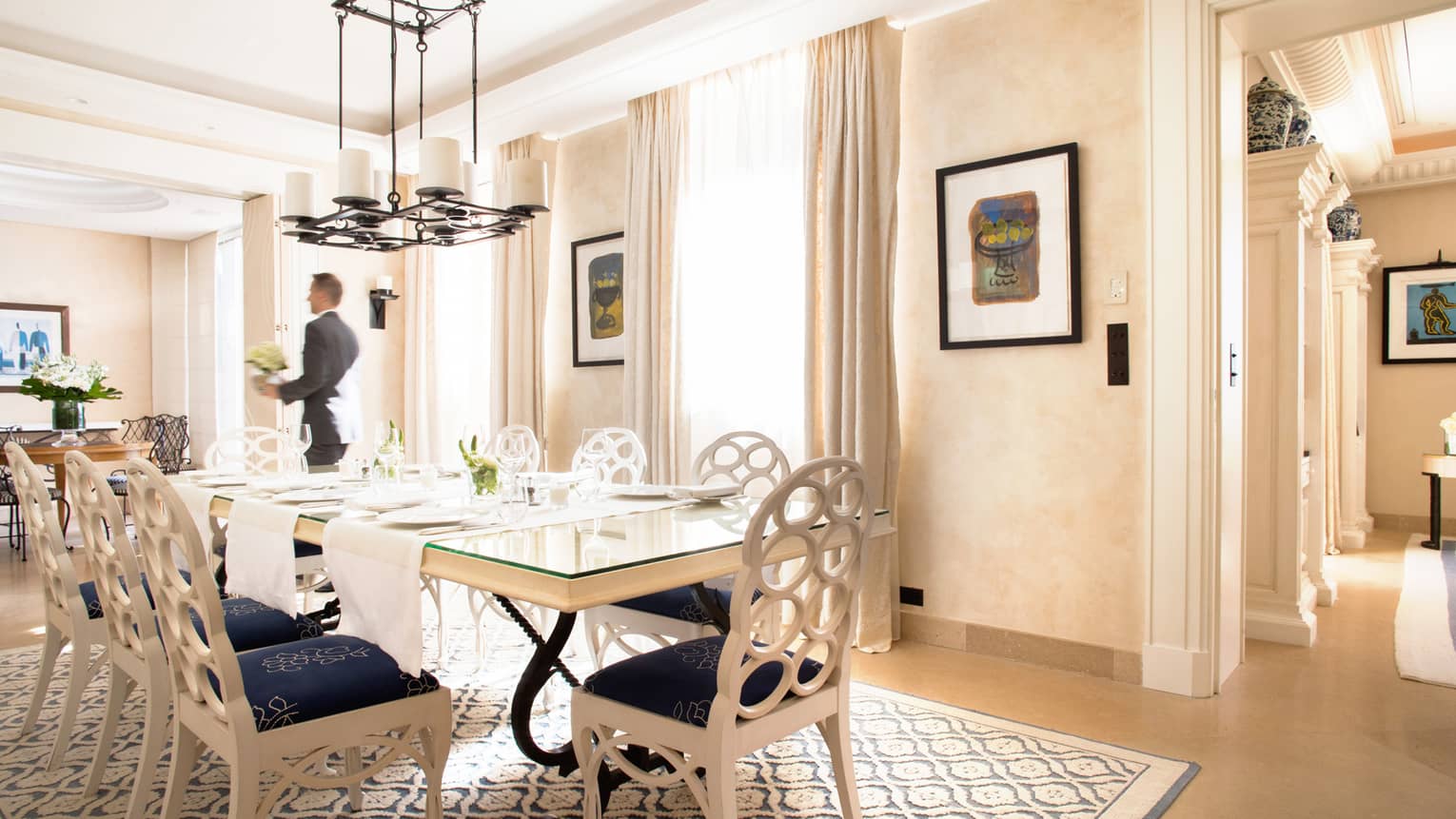 Hotel staff carries vase with flowers past long table in bright dining room