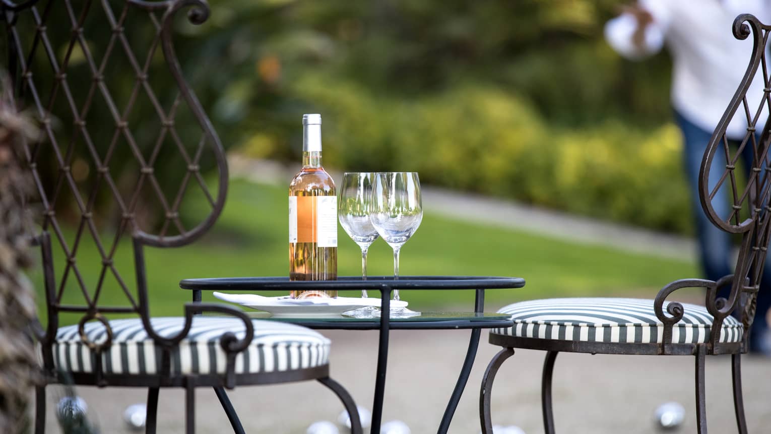 Close-up of bottle of wine, two wine glasses on iron patio table