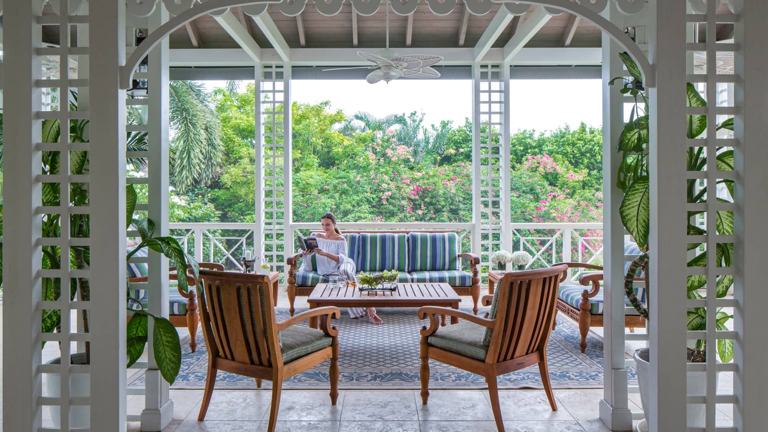 Woman reads book on plush patio sofa by chairs under awning