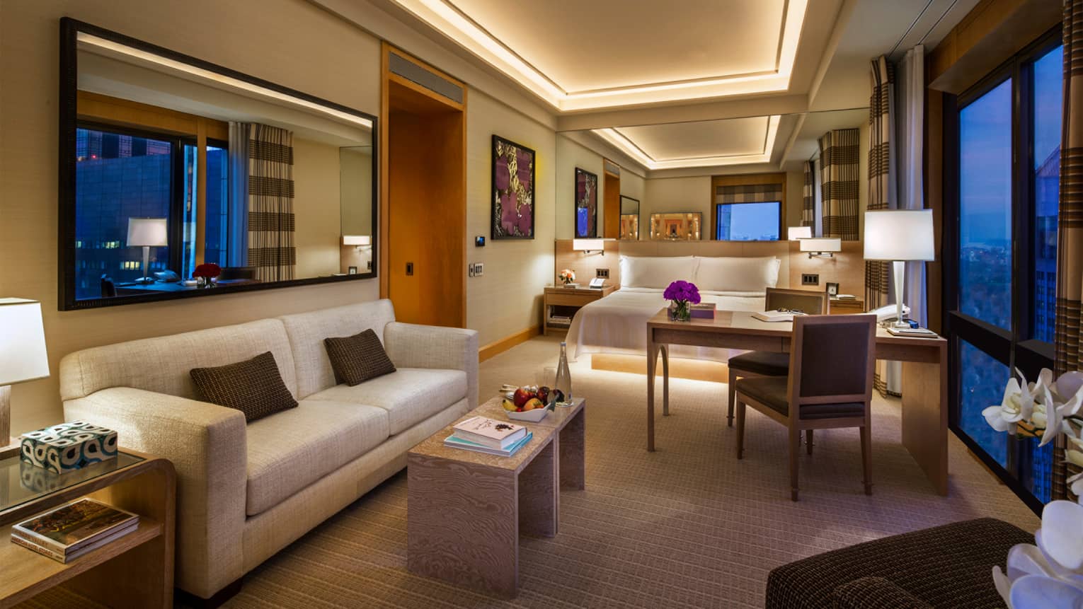 Gotham Junior Suite at night with white sofa, table, work desk by bed 