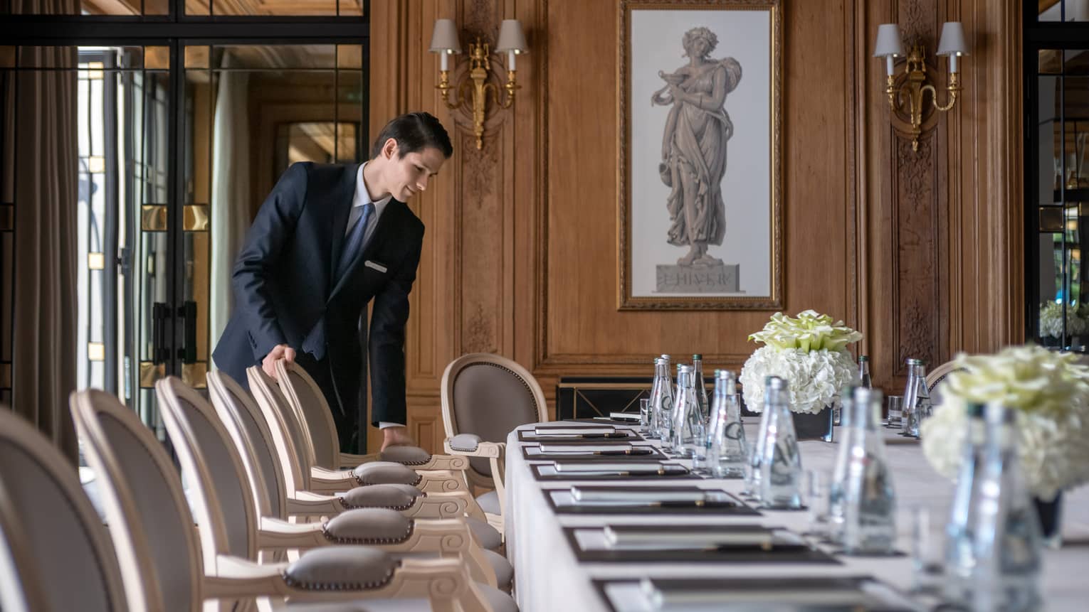 Hotel staff sets long table in Napoléon meeting room under framed print, wood wall