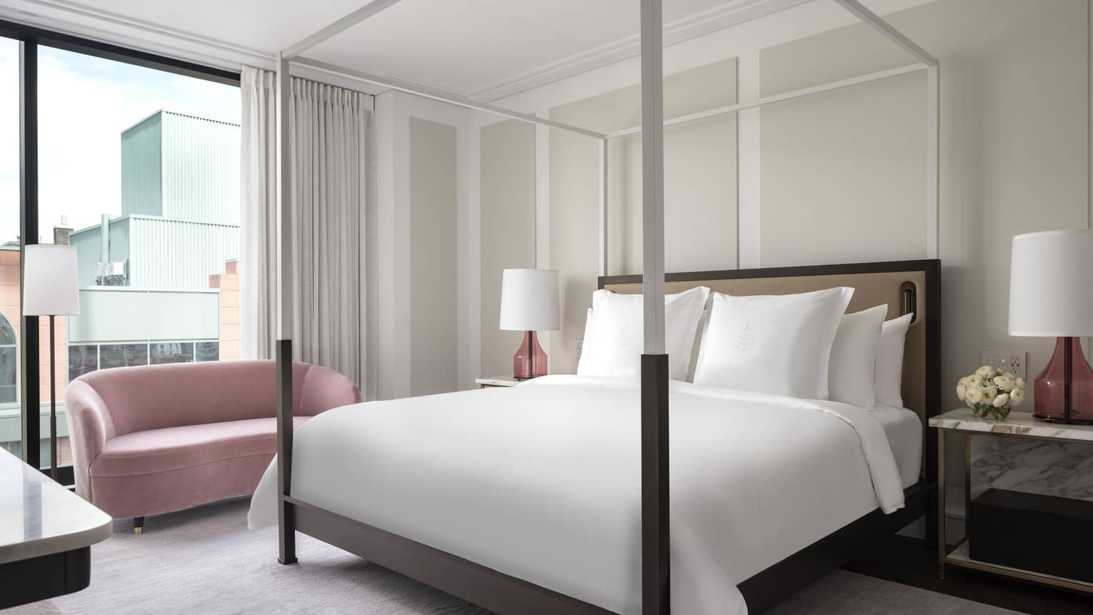Hotel room with modern four-poster king bed and pink love seat