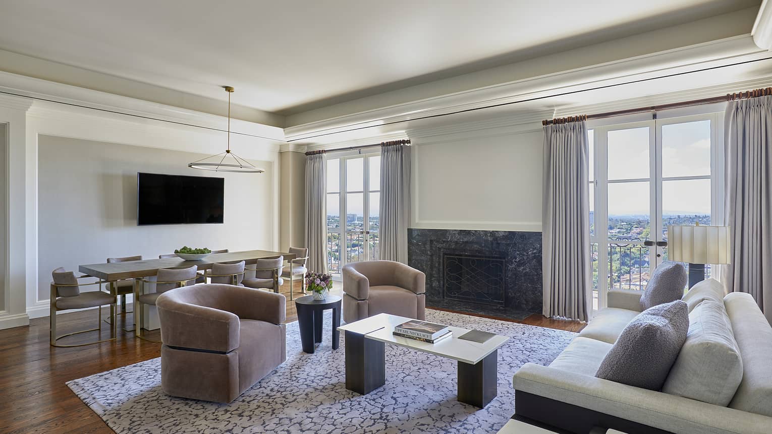 Living room with grey sofa, two mauve-coloured armchairs, dining table, two sets of glass French doors to a balcony
