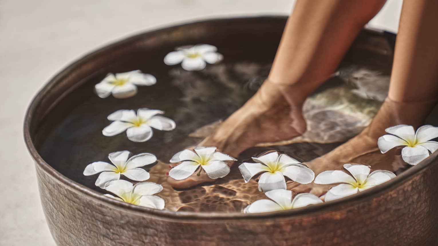 A woman's feet in a bowl of water and flowers.