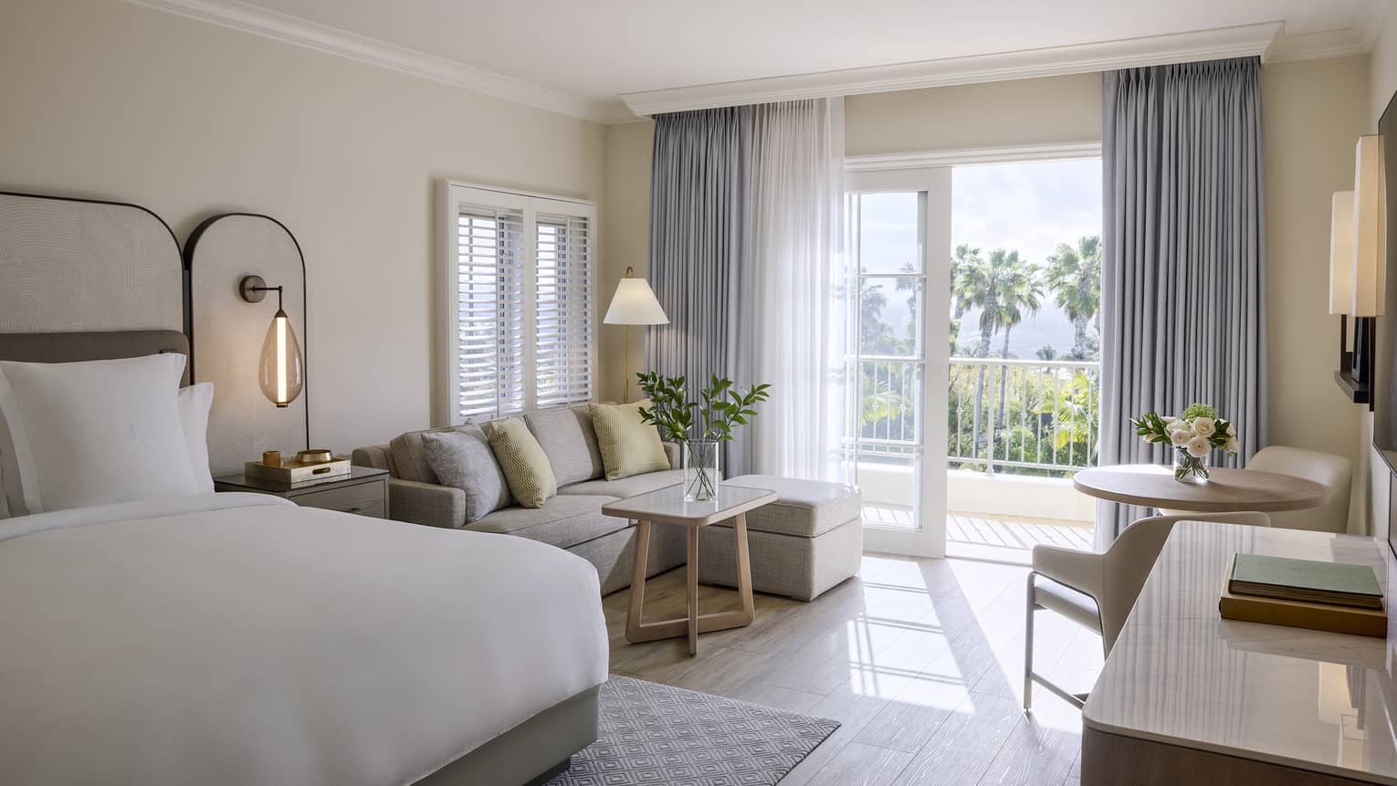 Elegant residential room with king bed, sitting area with sofa, table with two chairs, and balcony