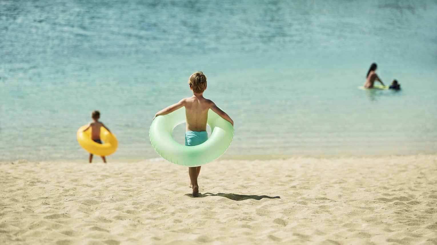 A young boy holds a floaty ring and runs into ocean on beach