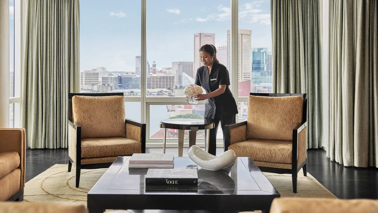 Woman cleaning a living room, with four gold-coloured, upholstered arm chairs, large coffee table