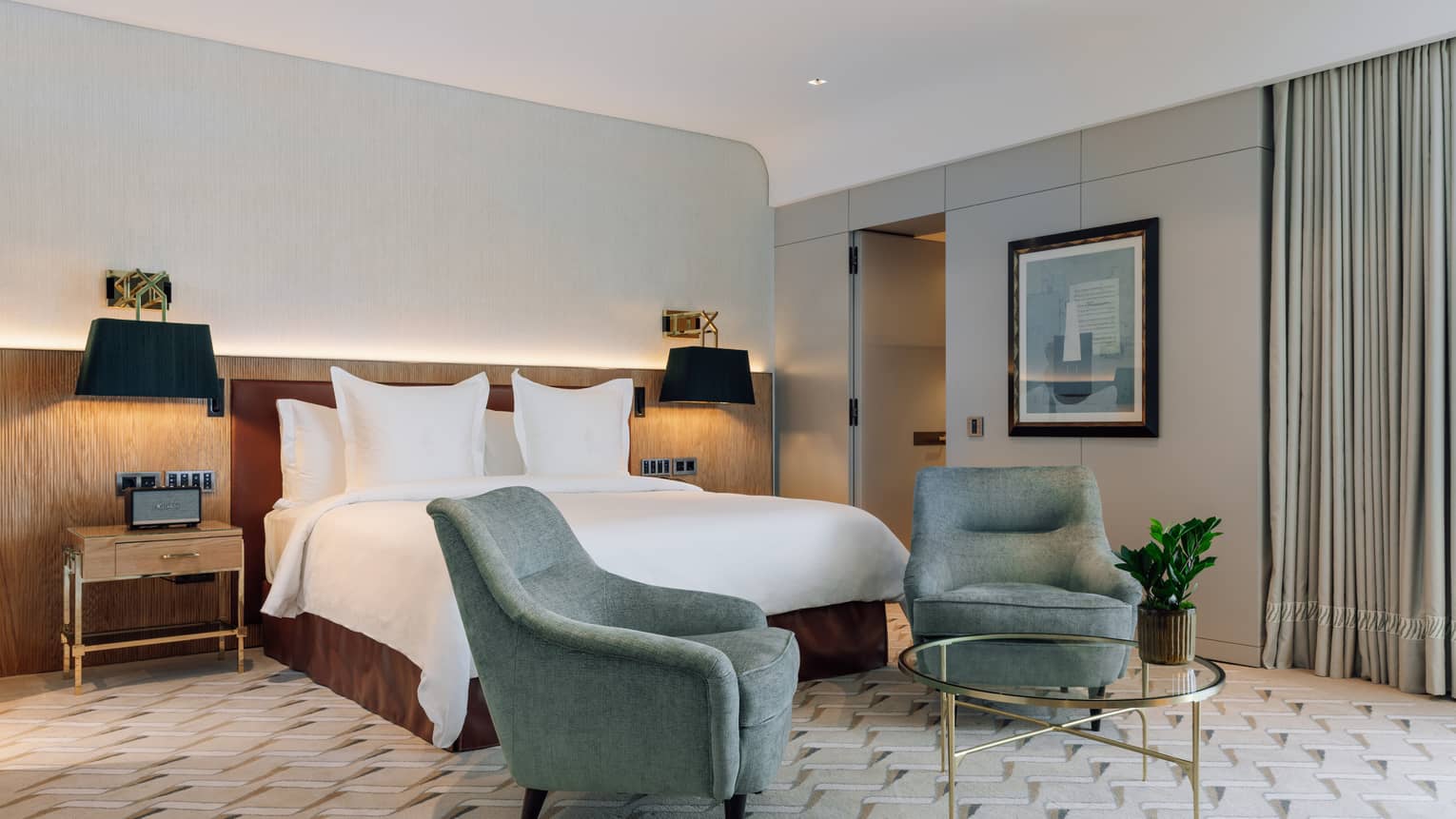 Hotel room with king bed, two turquoise arm chairs and brass glass table