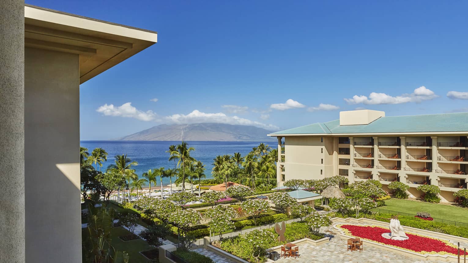 Resort courtyard with gardens and fountain overlooking palm trees beach and ocean with mountain in the distance