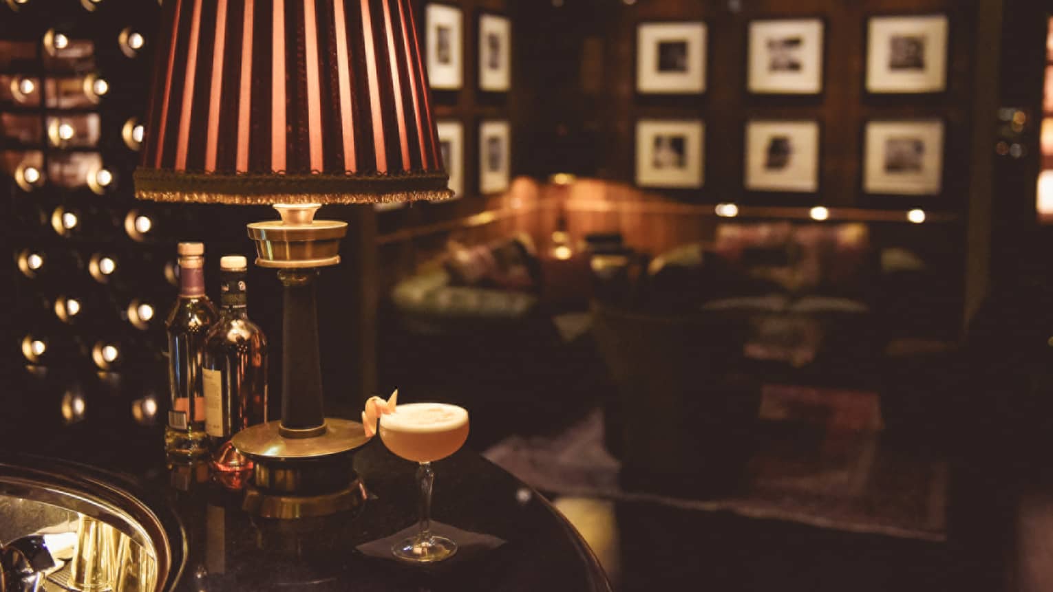 Close-up of small lamp, cocktail glass with lemon peel garnish on bar in dark lounge 