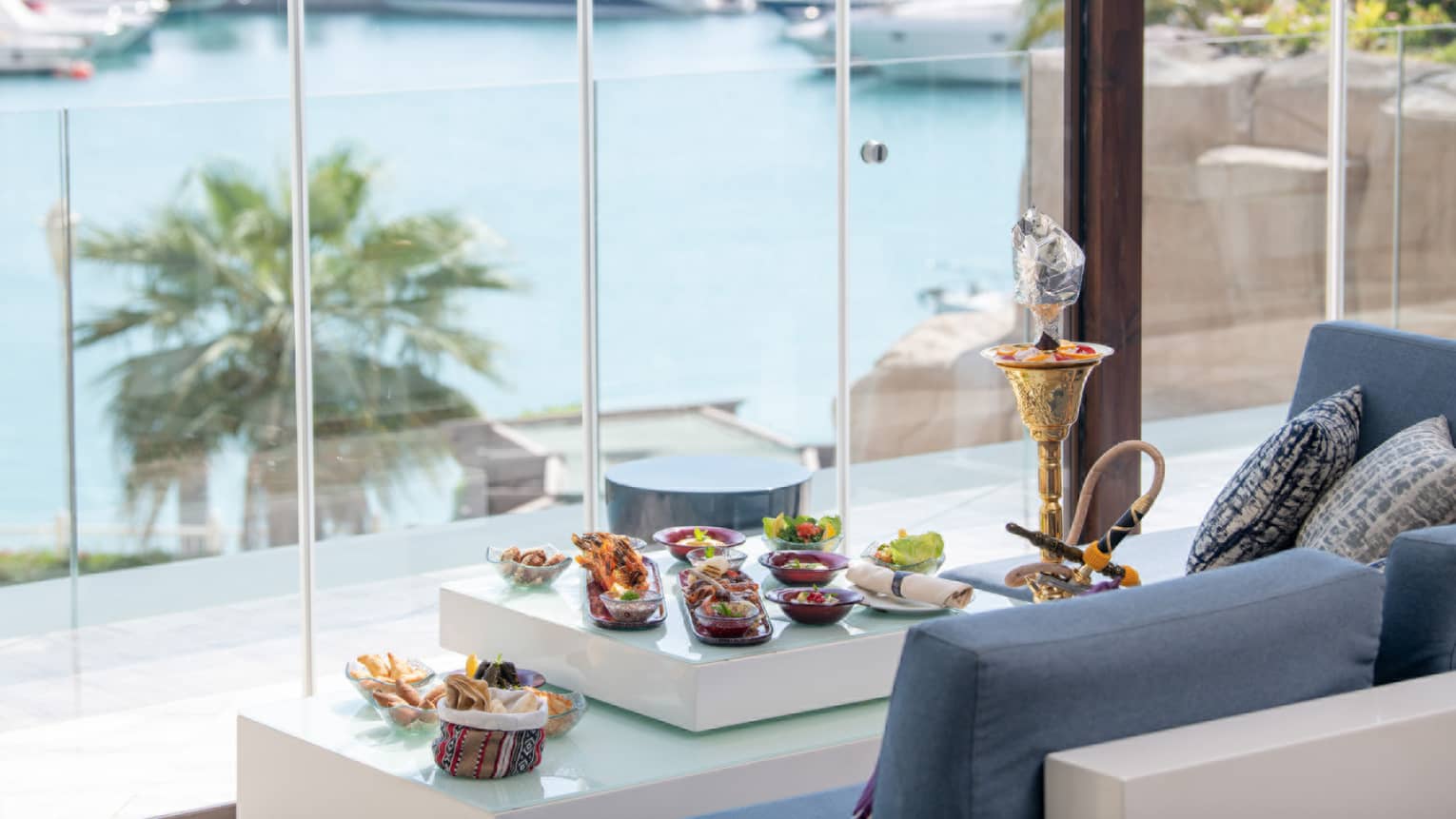 View of the marina through floor-to-ceiling windows at The Terrace, shisha and canap�s on table in front of blue sofa lounge