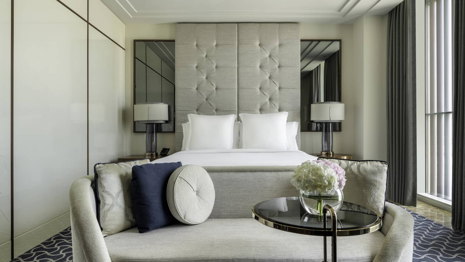 Hotel room with king bed, ceiling-height upholstered headboard, beige chaise and floor-to-ceiling windows