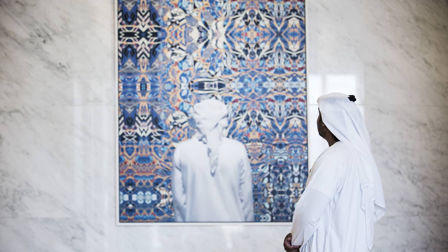 Side view of man dressed in white looking at colourful painting on white marble wall