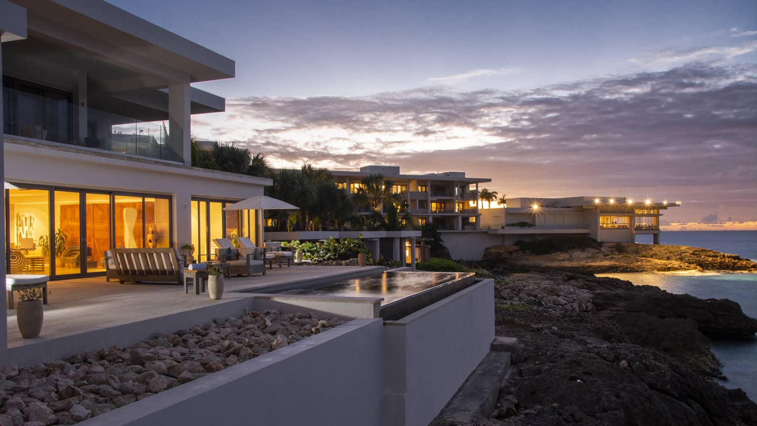 The exterior of a beachside hotel with orange lights coming from floor to ceiling windows.