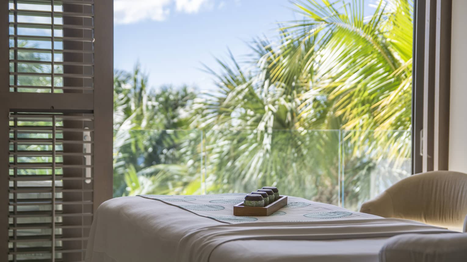 A massage bed near an open window with palm trees outside.