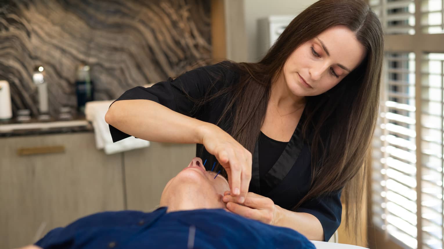 Woman performs acupuncture on person's face at luxury resort spa