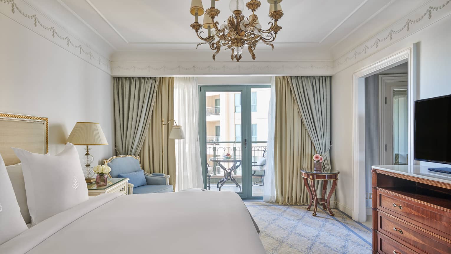 Four Seasons Suite bedroom with king bed, blue corner chaise longue, glass door to veranda, chandelier