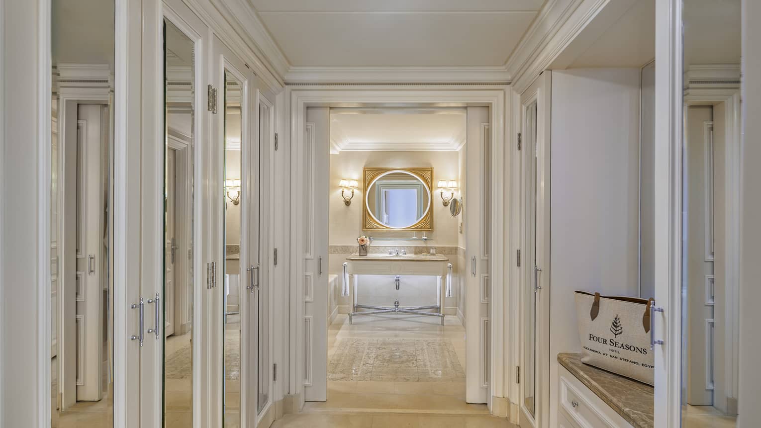 Four Seasons Suite mirrored hallway leading to bathroom with single vanity, lighted wall sconces, oval mirror