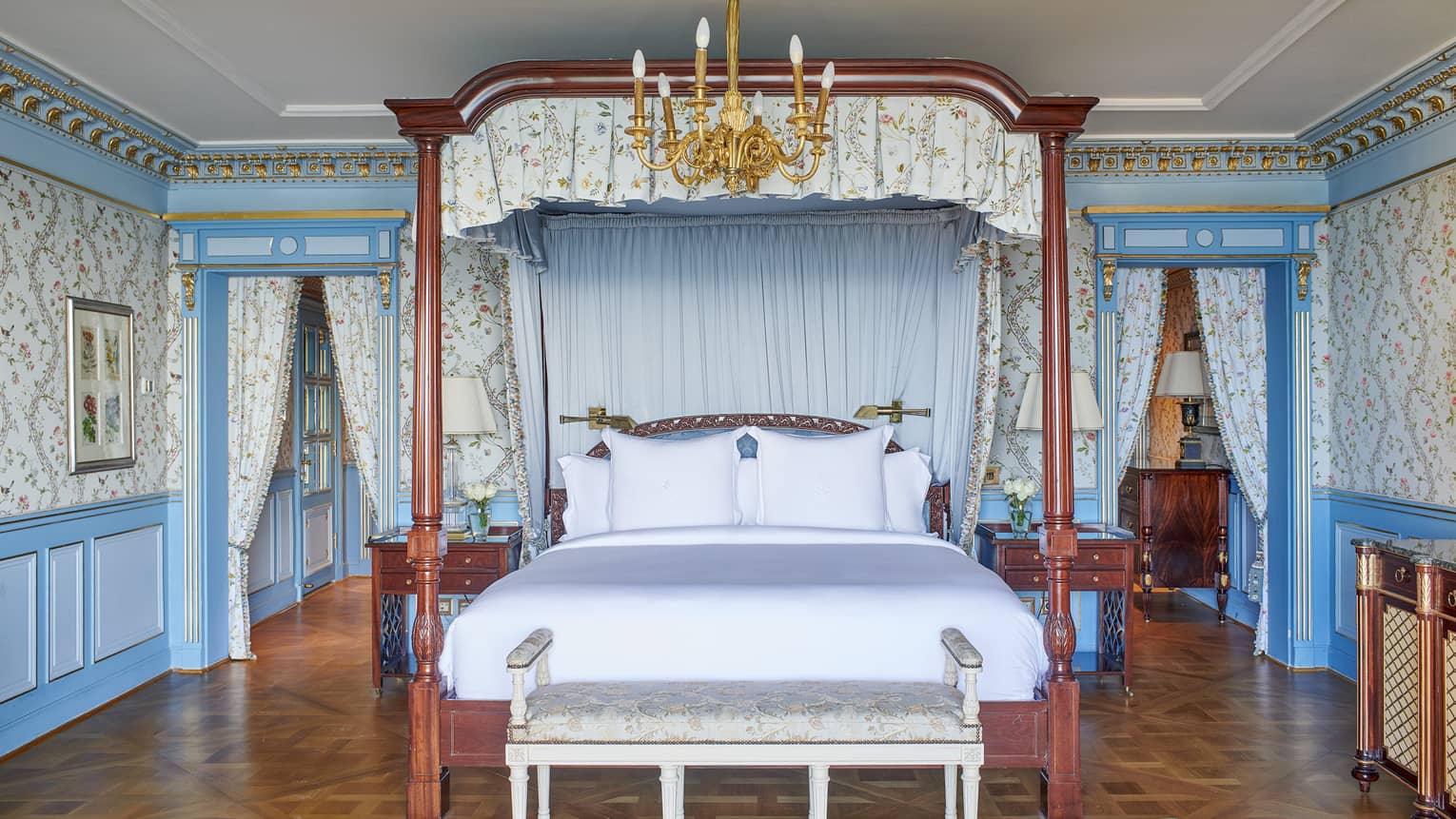 Presidential Suite bedroom with four-poster king bed, blue wall accents, paisley wallpaper, chandelier, parquet flooring