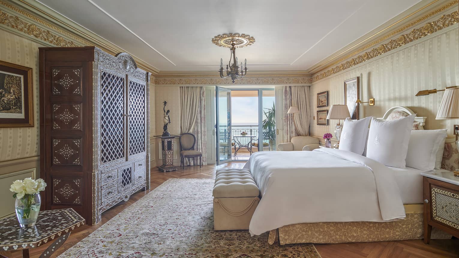 Royal Suite bedroom with king bed, oak armoire, corner armchair, glass door to veranda
