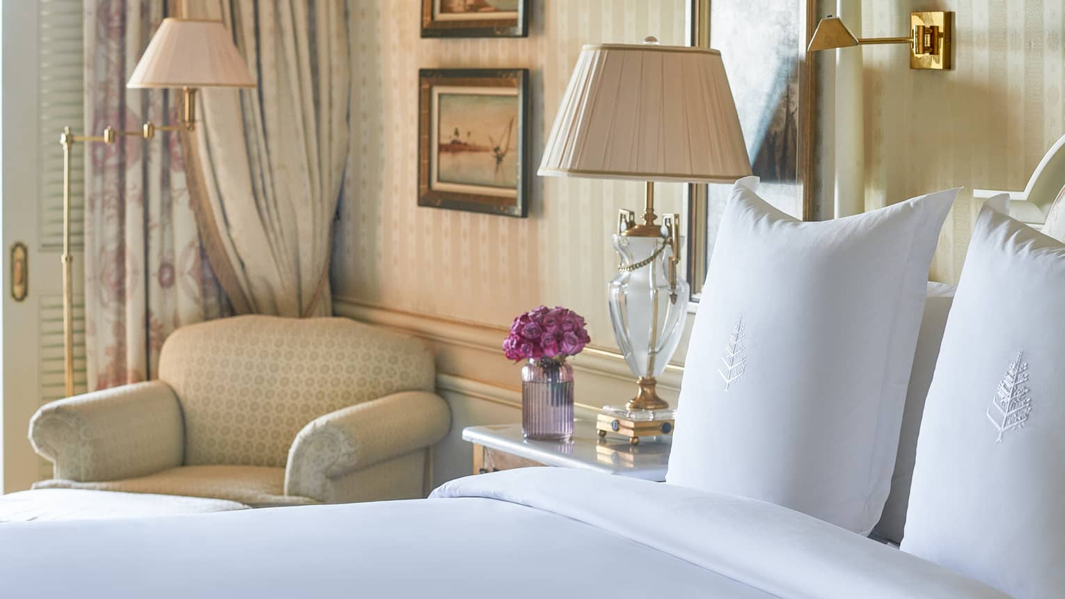 Close-up of bed with white linens, corner armchair, side table