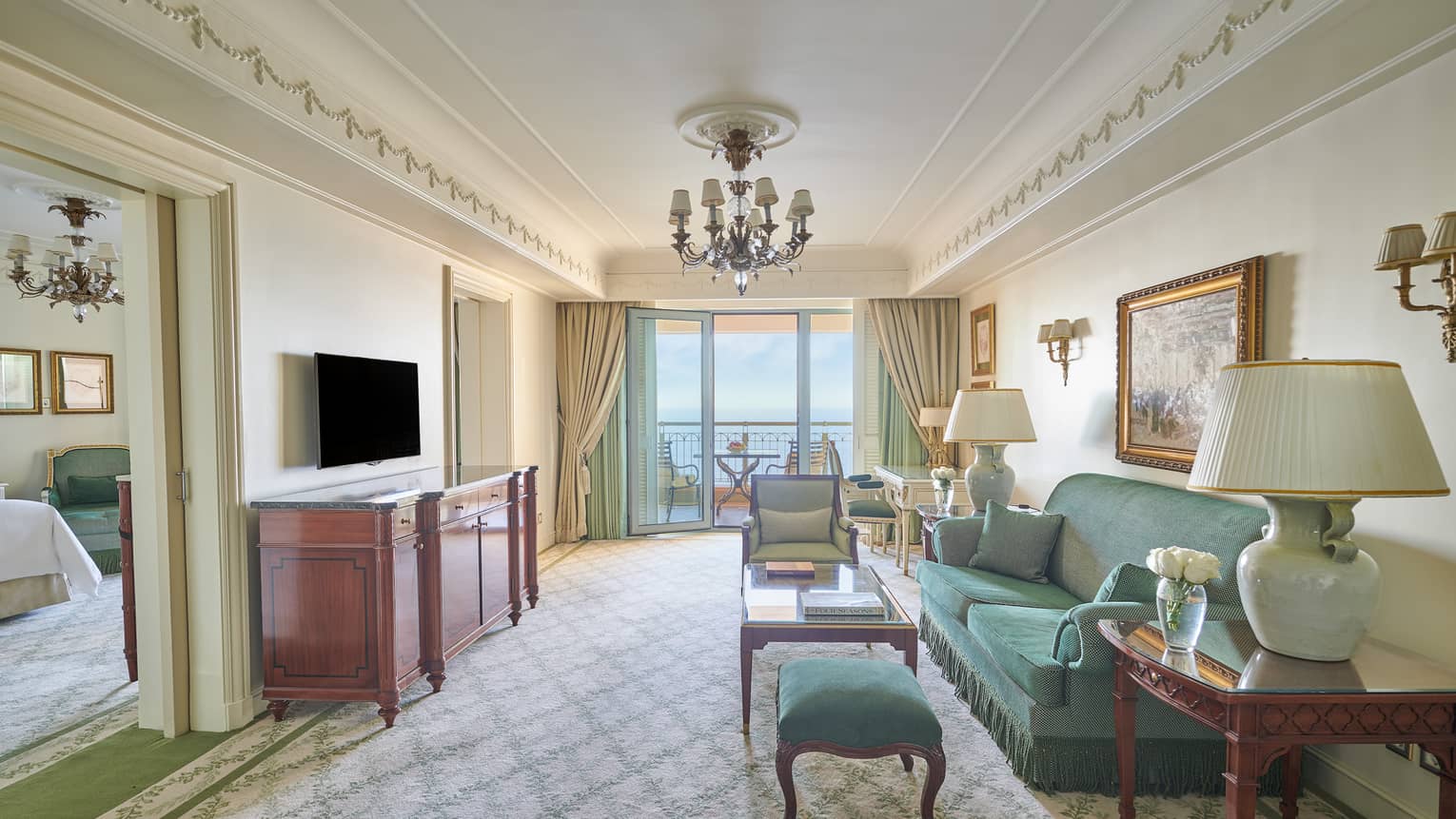Sea View Suite living area with green sofa, armchair, side tables with lamps, glass door to veranda, bedroom visible through doorway
