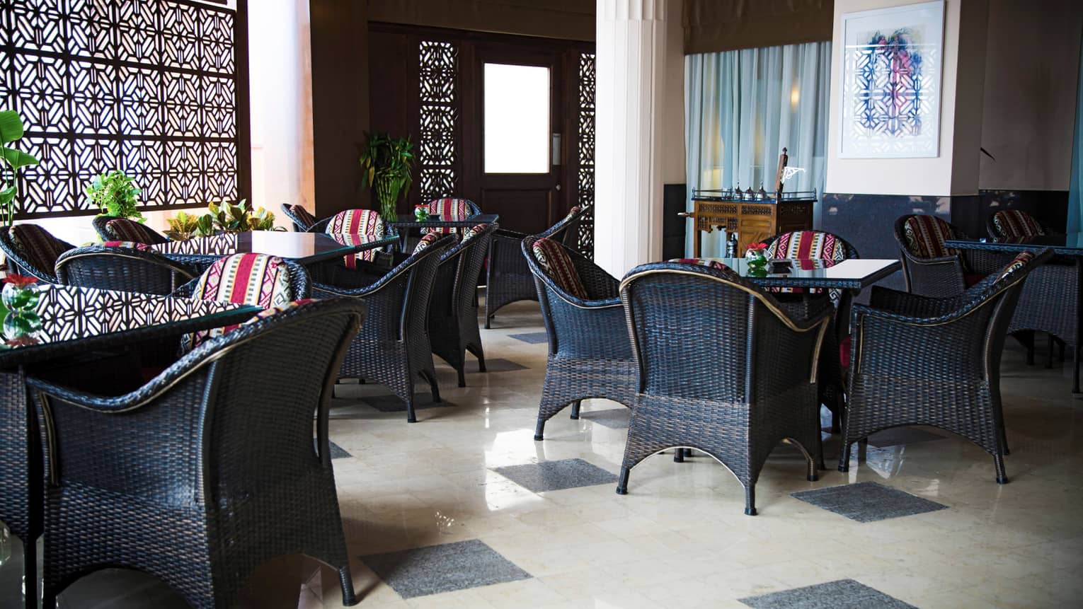 Dining room with two white pillars, three black square tables, each with four black chairs, black and white tile floor