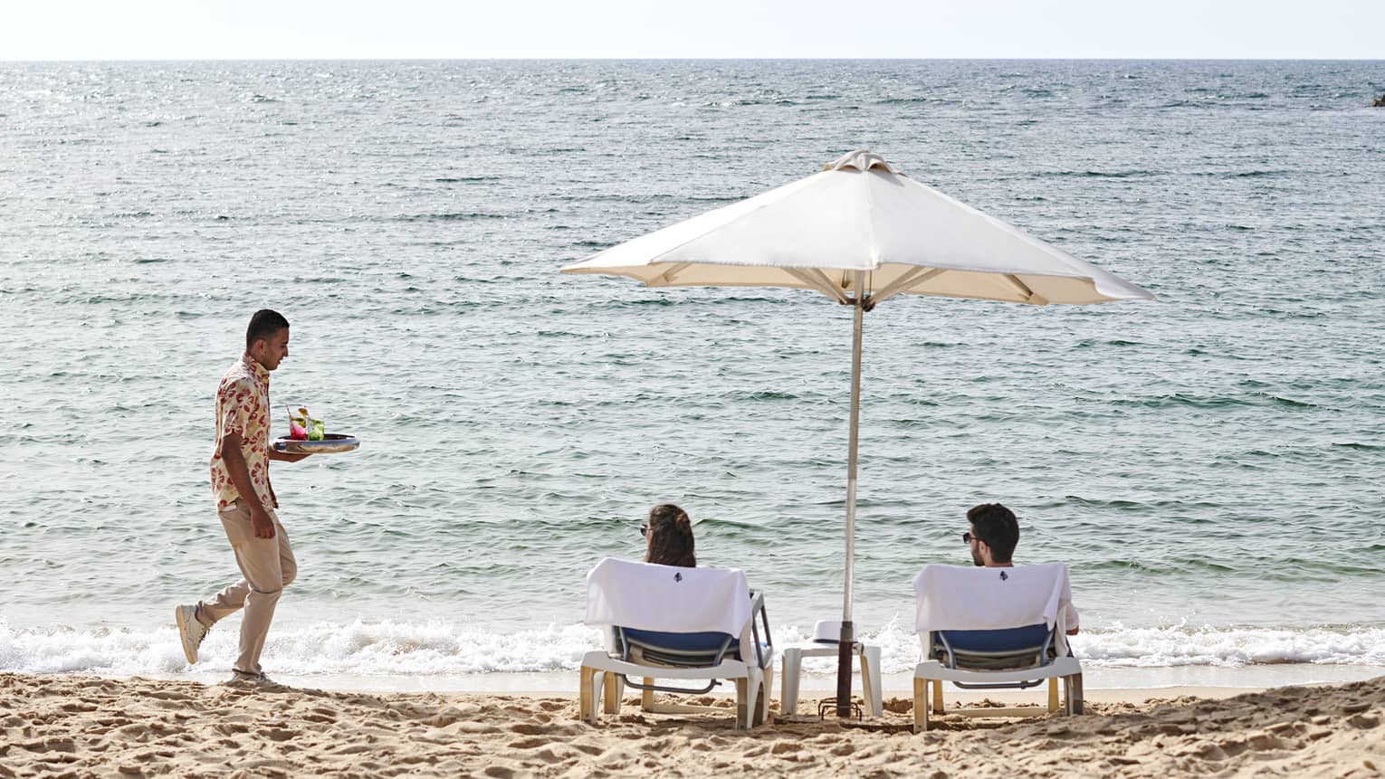 a couple lounges on the beach in alexandria while a four seasons staff serves them refreshments