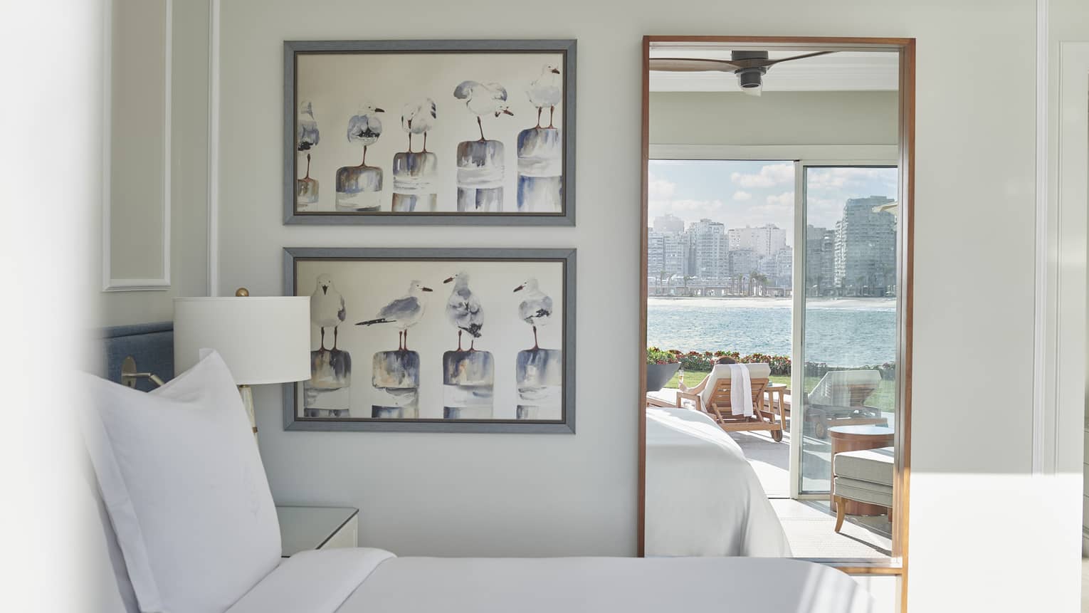 White-sheet bed, two framed pictures on wall, standing mirror