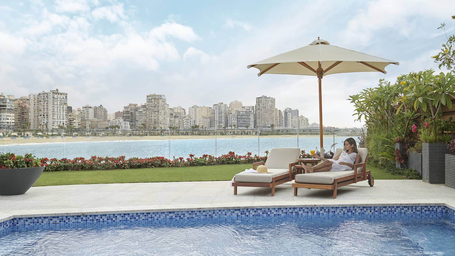 Woman lays on lounge chair under umbrella by sea-view pool