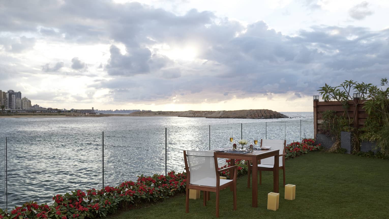 Small wooden dining table and two chairs set on lawn next to sea