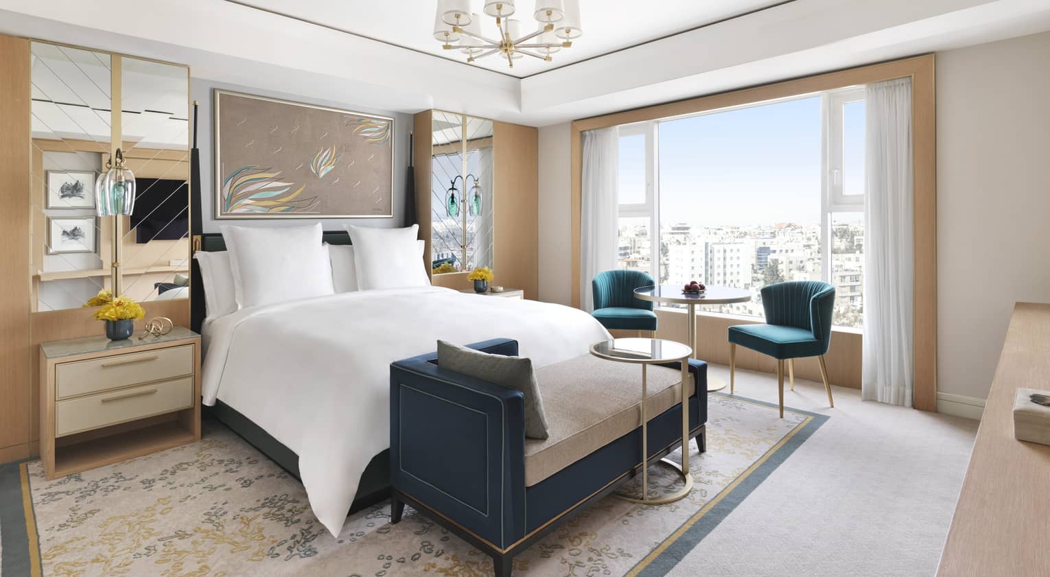 A bed in the centre of a cream coloured room with a chaise perched at the end of the bed. 