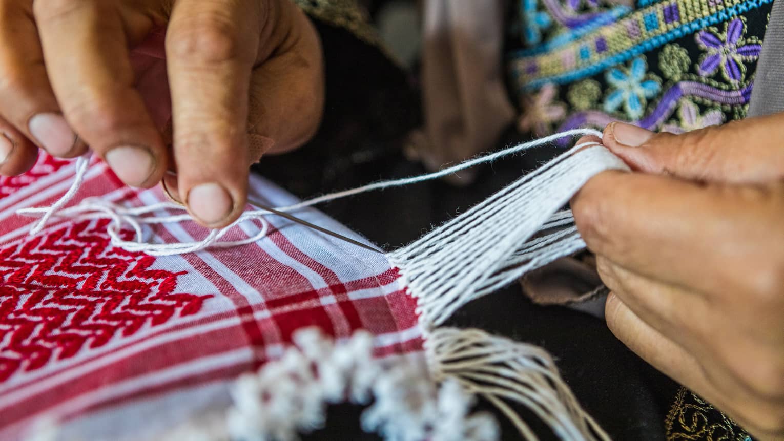 A person weaving strands of fabric together to create a quilt.