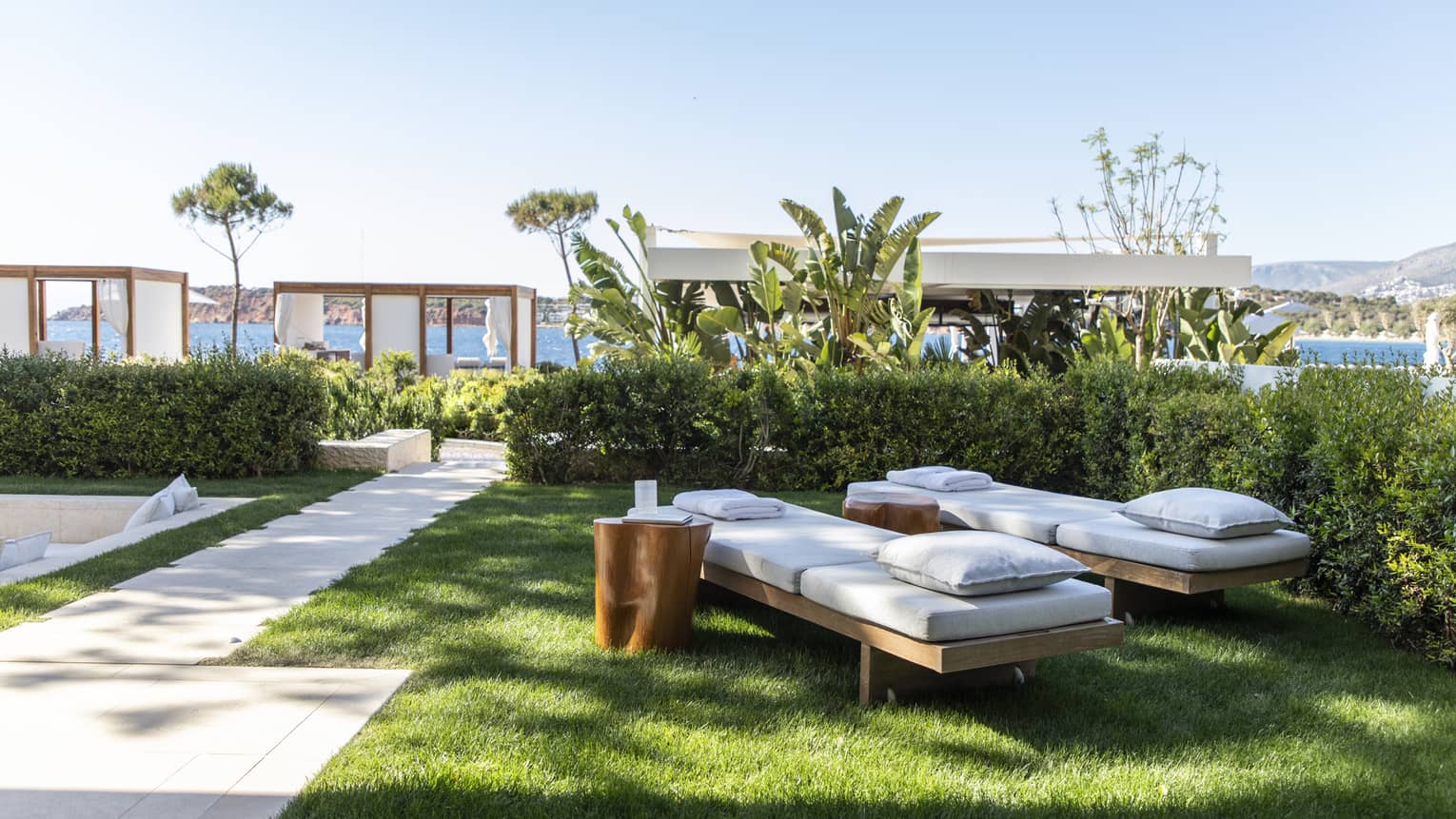 Private garden with two chaise lounges set on the grass, beach cabanas visible in the distance