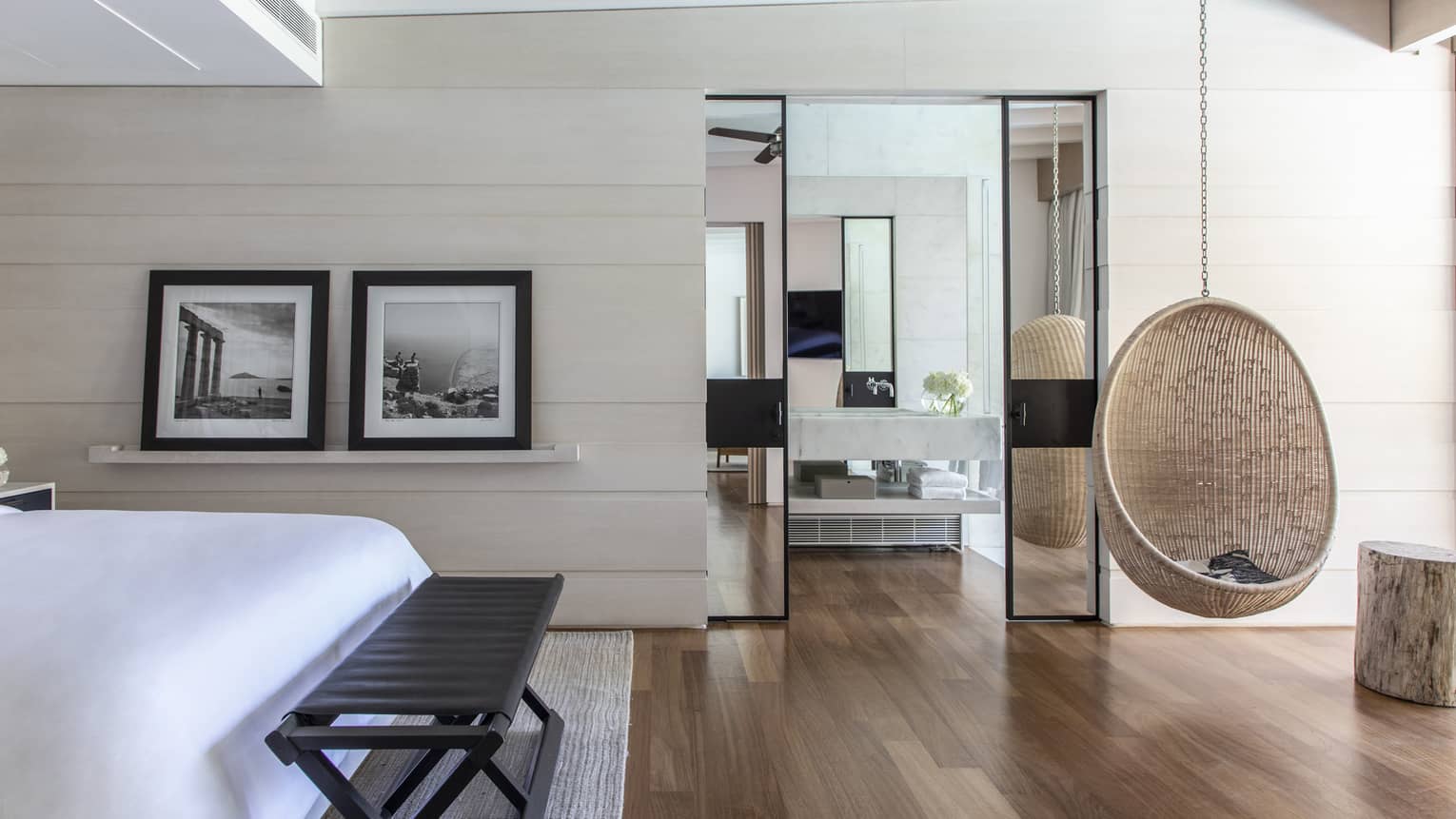 Bedroom with hardwood floors, hanging whicker chair, two framed photos, bench
