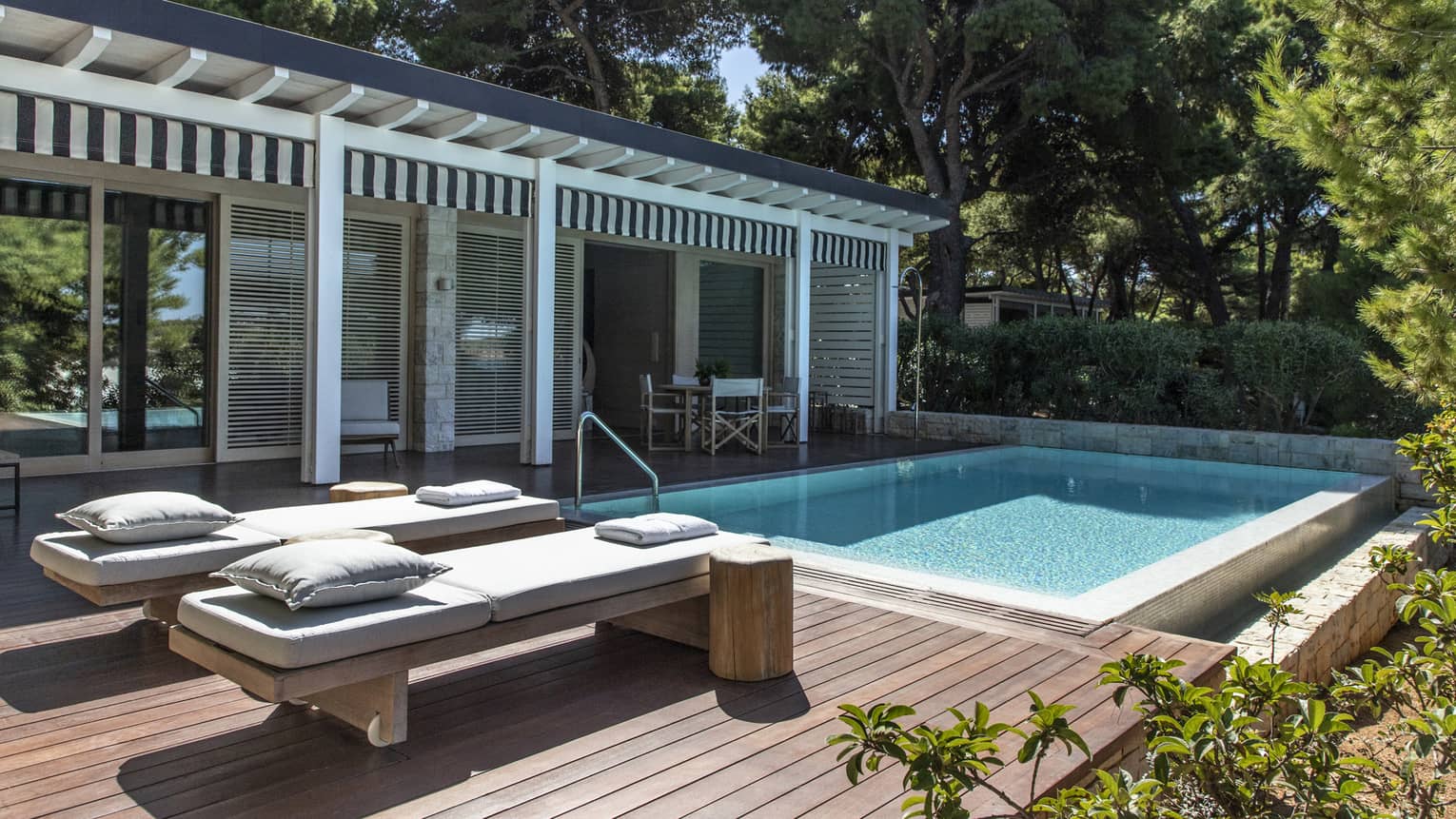 Private wooden deck with two lounge chairs and pool, surrounded by greenery,Private outdoor pool with luxurious sun loungers, contemporary pergola design and lush greenery, offering a private retreat and serene sea views