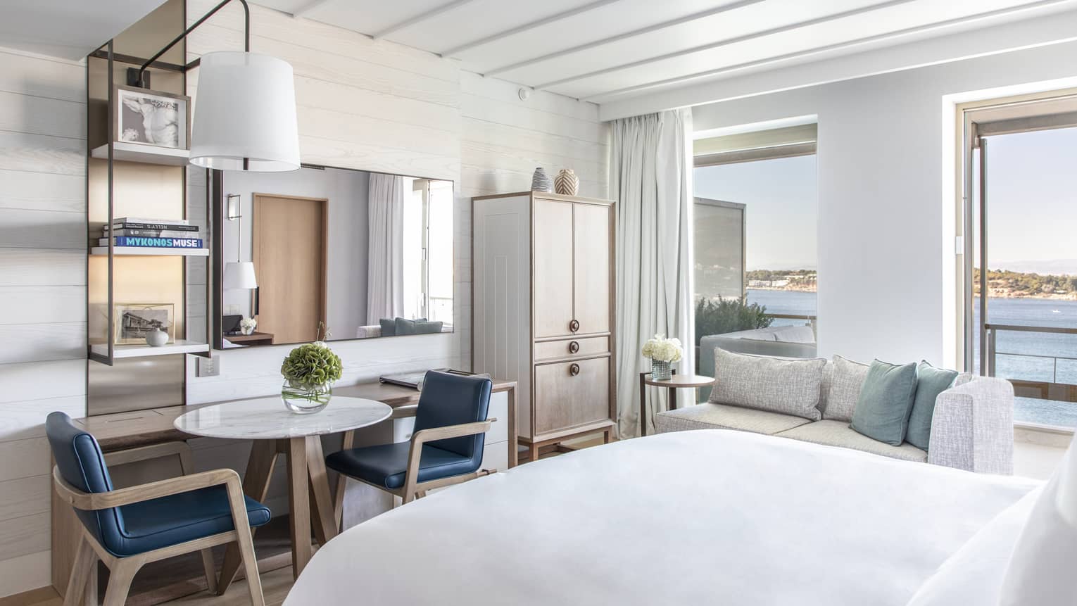 Bedroom with small table, two blue chairs, wall-mounted lamp, sea views