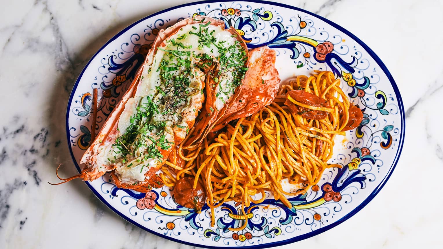 Half lobster sprinkled with herbs beside spaghetti with chilli and garlic on colourful plate