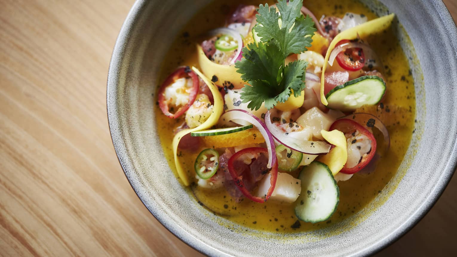 A gray ceramic bowl of a vegetable, curry soup garnished with cilantro and jalapenos 