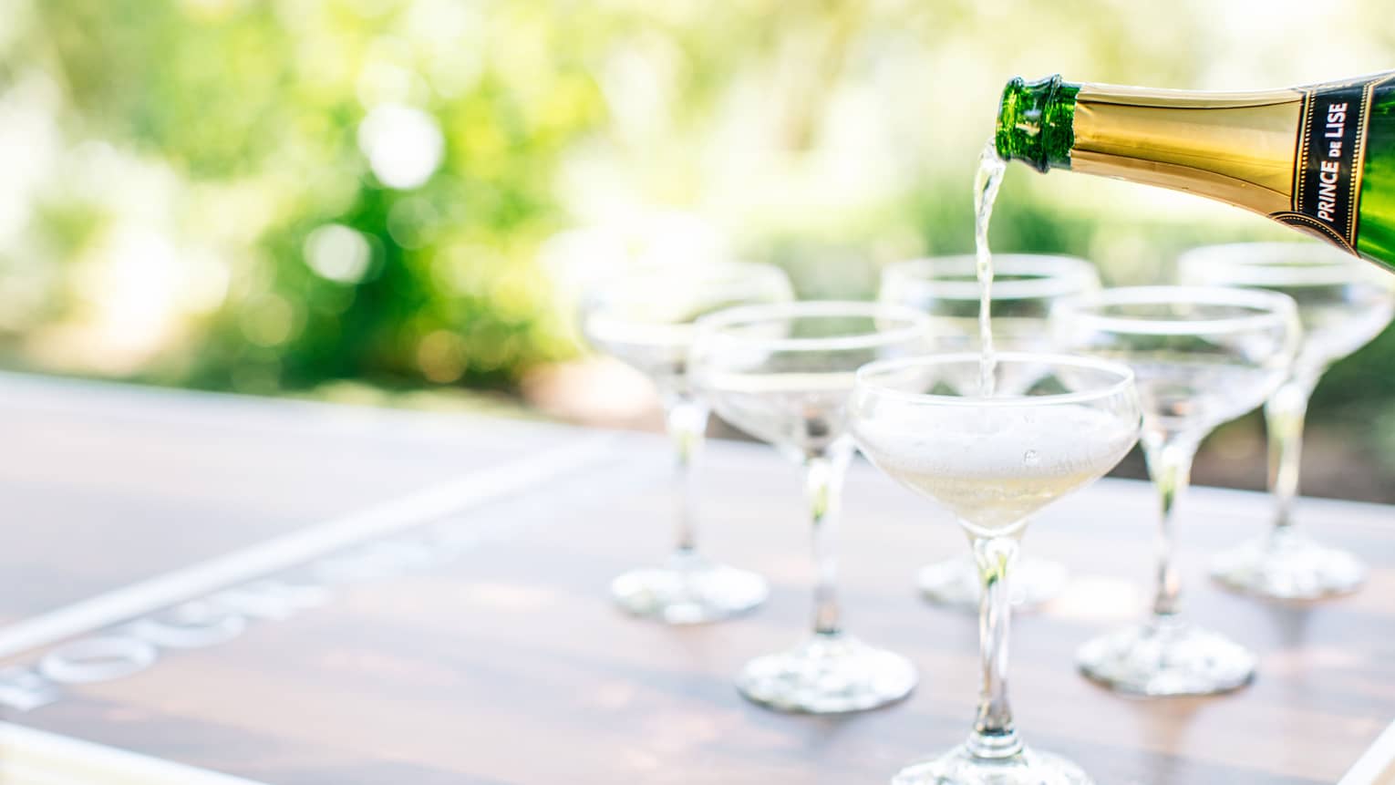 Sparkling wine being poured into wine glasses outside.