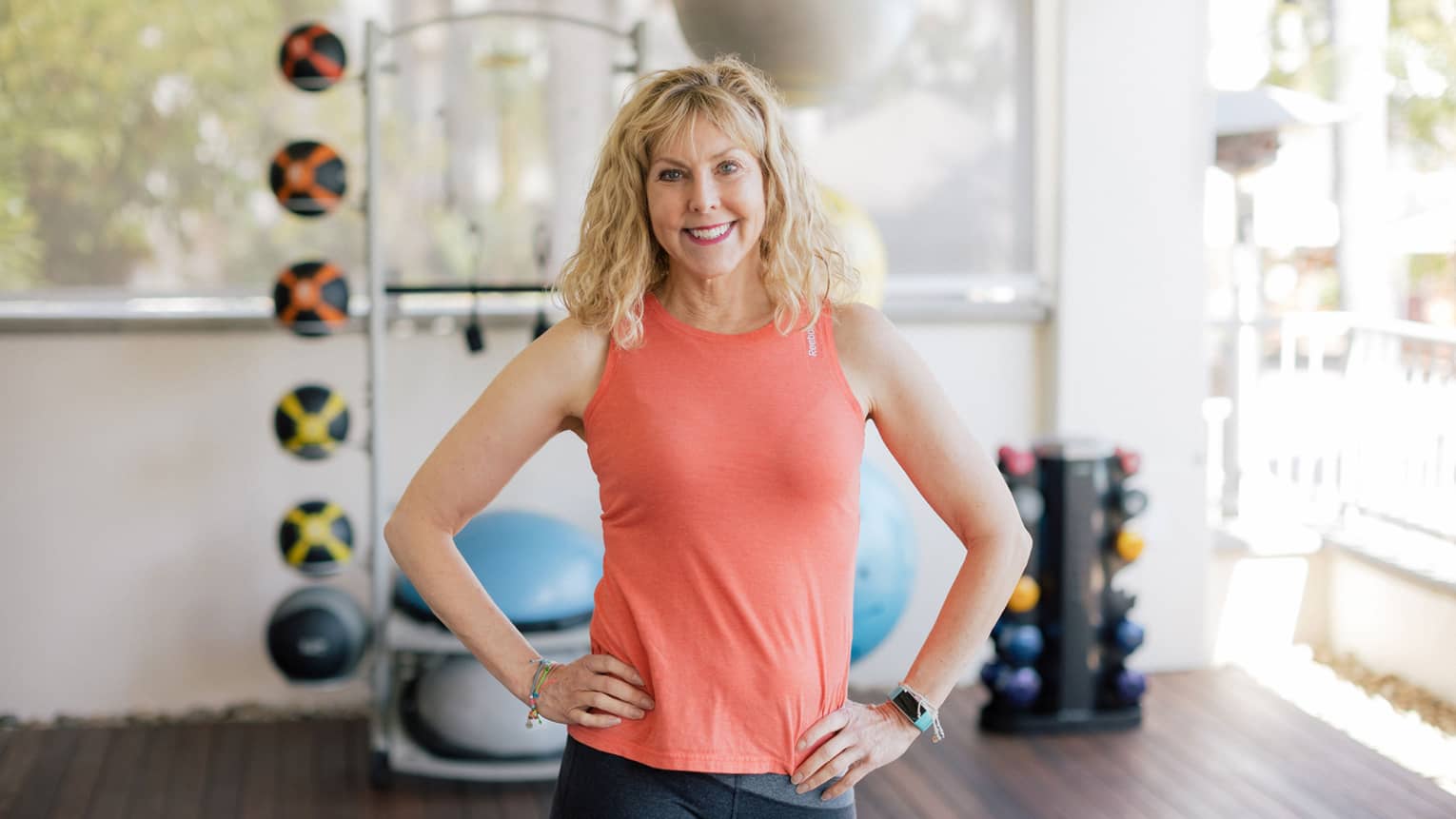 A woman standing in front of exercise balls and large windows.