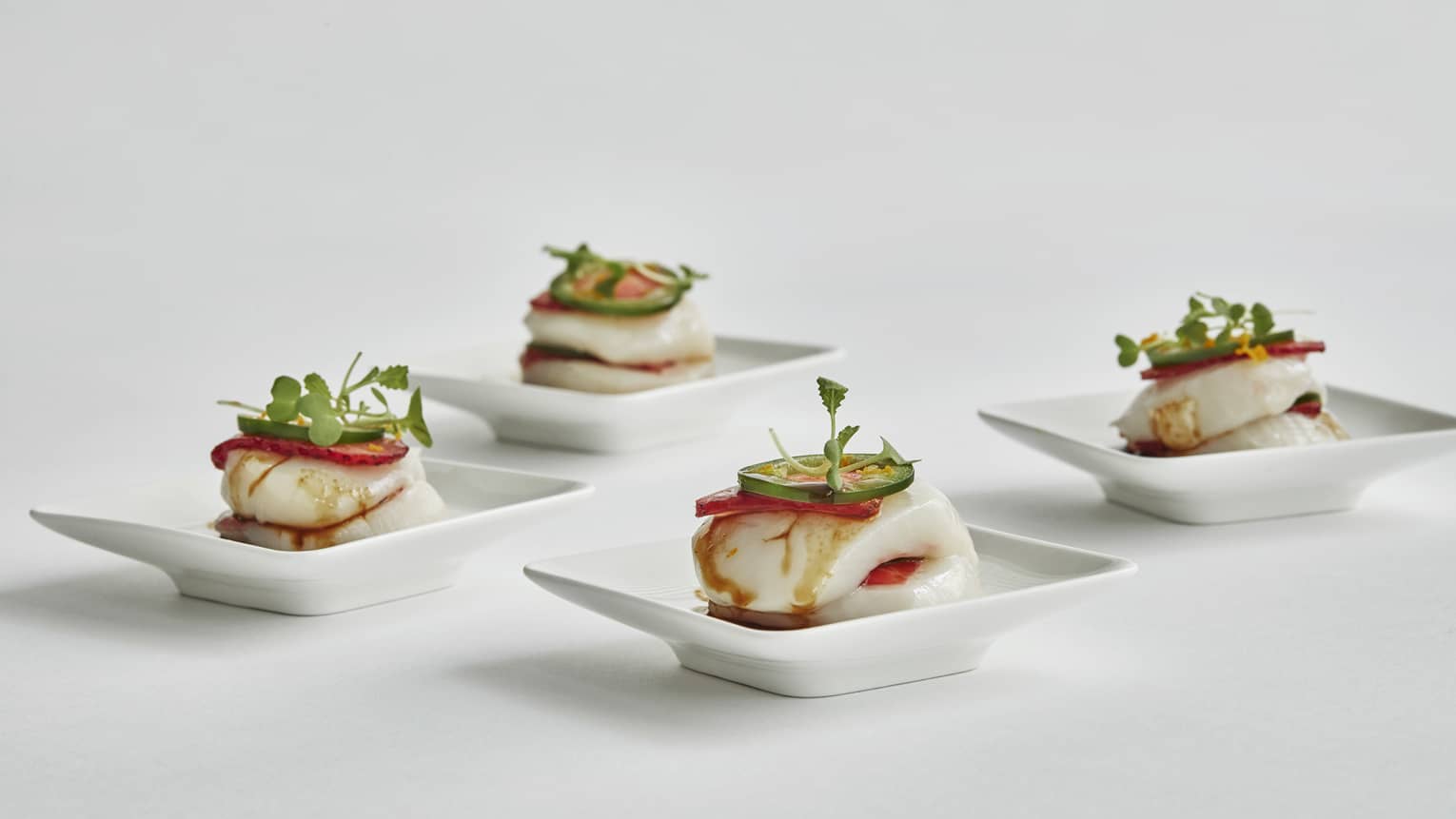 Four small plates of scallop looking dishes topped with sprouts