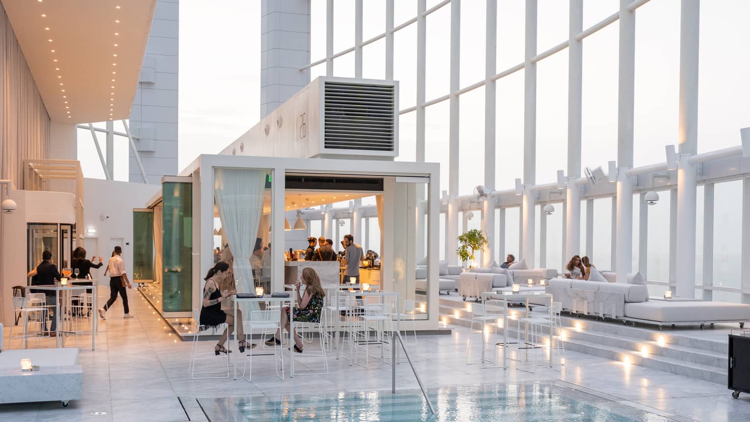 People mingle around a contemporary white bar next to pool