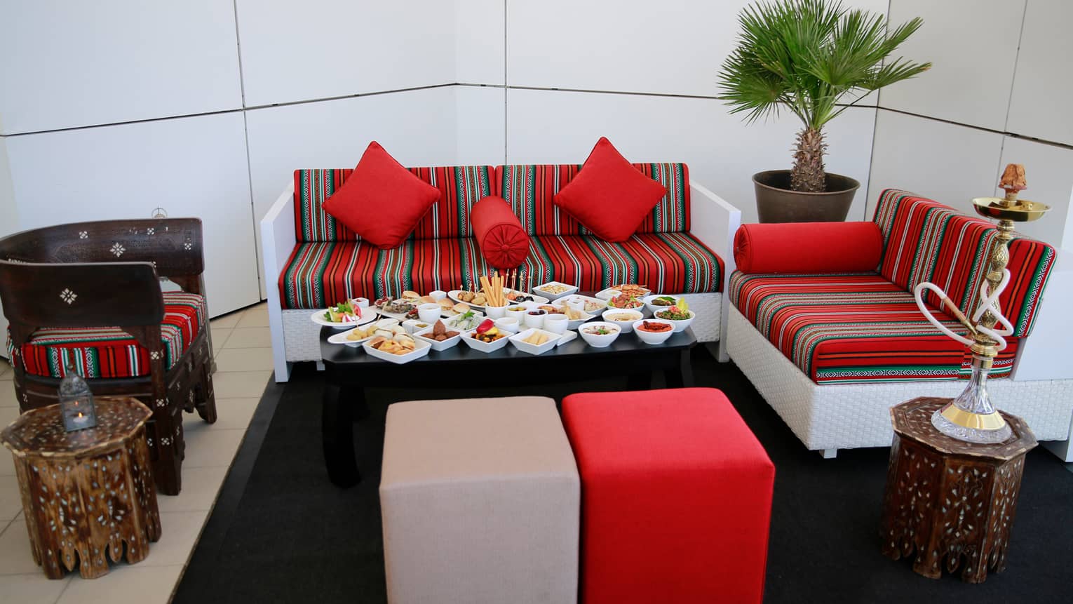 Close-up of small black table with more than a dozen white dishes with mezze appetizers and snacks, colourful striped sofa
