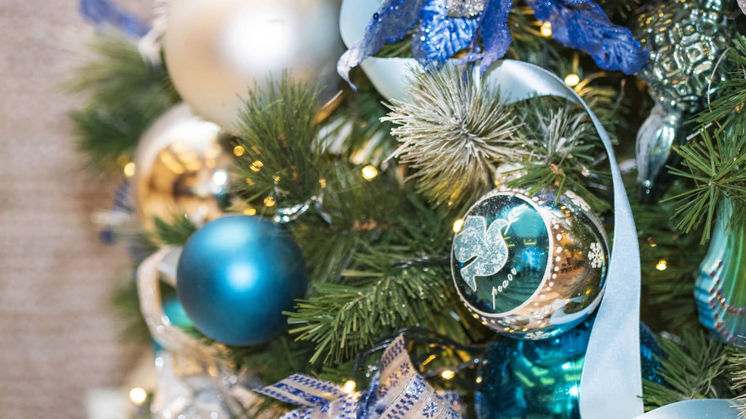 A close up of a Christmas tree decorated with orante blue and silver ornaments, clear lights, and blue ribbon