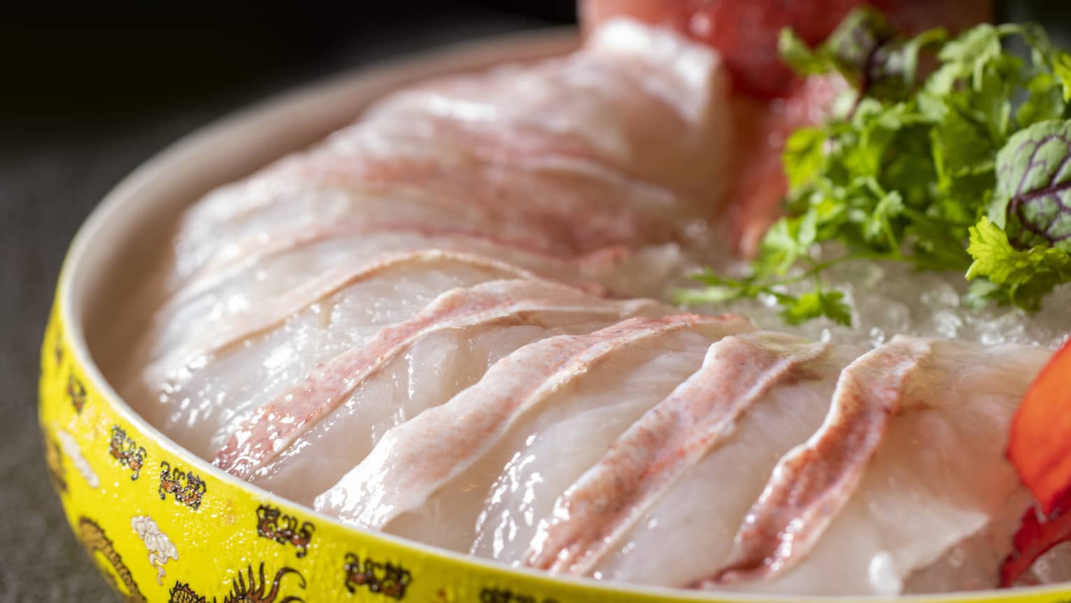Slices of white fish on ice in yellow dish with green garnish
